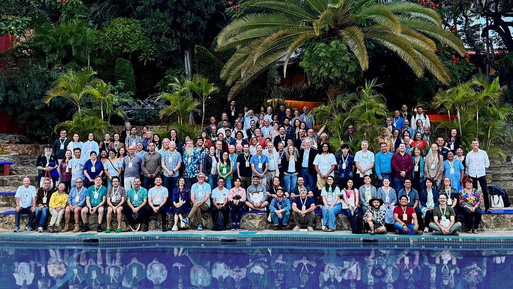 Attendees at the International Oak society conference Mexico 2025. A large group of people in front of palm trees, next to a swimming pool.